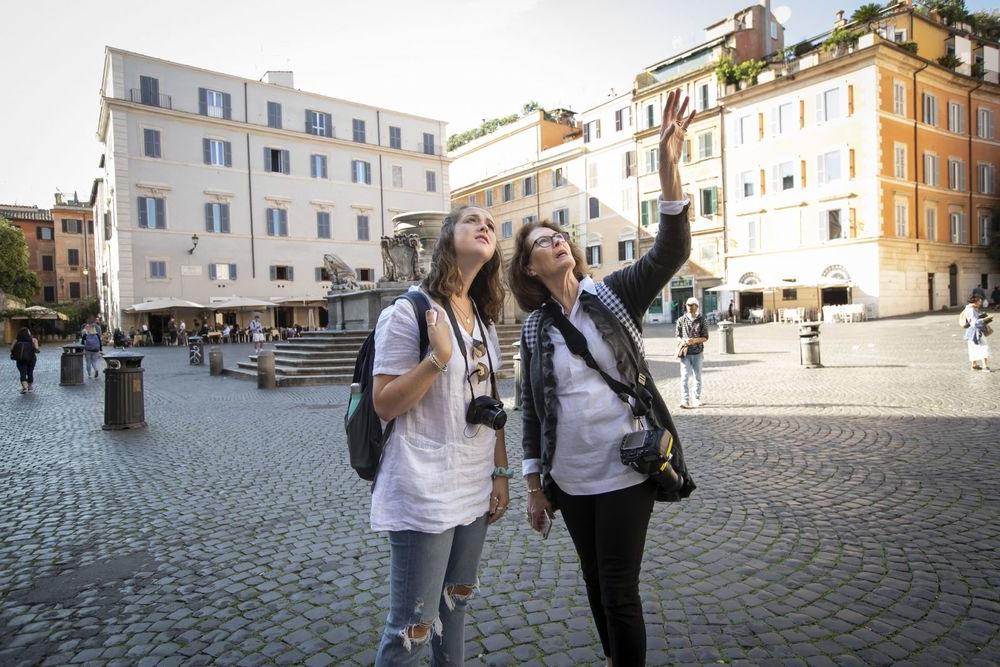 A professor and student with cameras around their necks observe their surroundings in an Italian piazza.