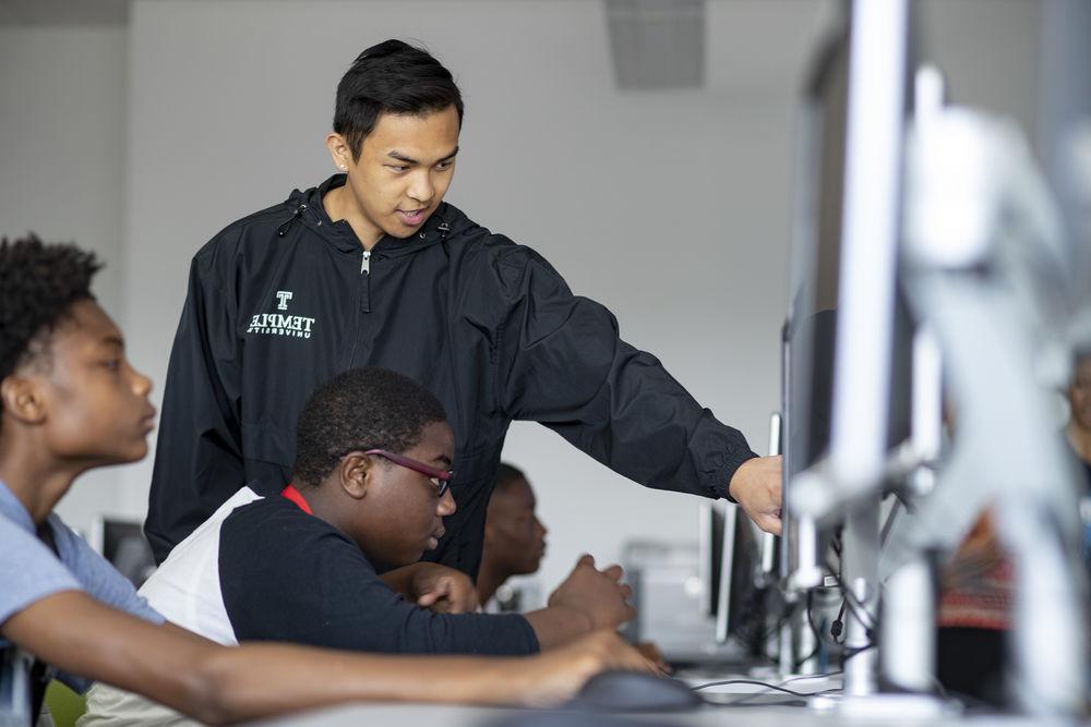 CST student instructs secondary school students on desktop computer. 