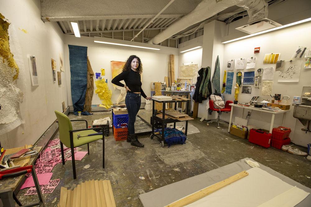 A student in black clothing paints in an art studio. 